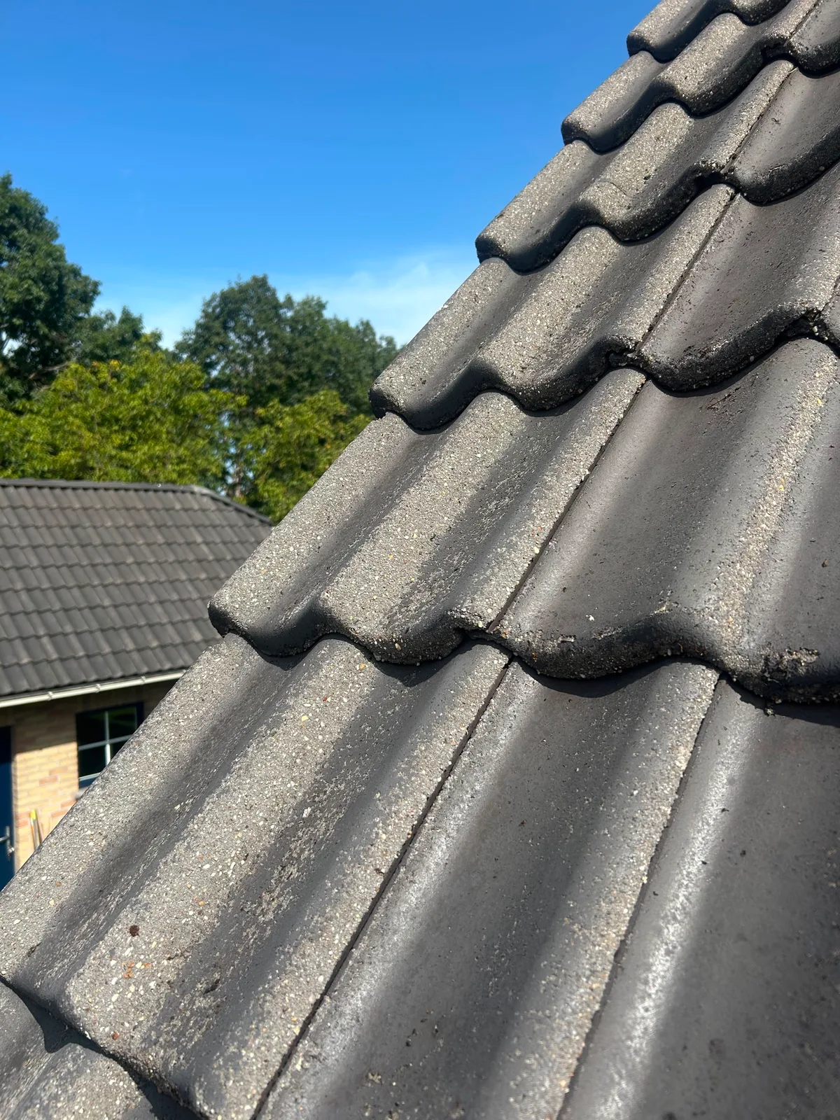 Dezelfde dakpannen na het ontmossen: schone donkergrijze pannen zonder mos of aanslag